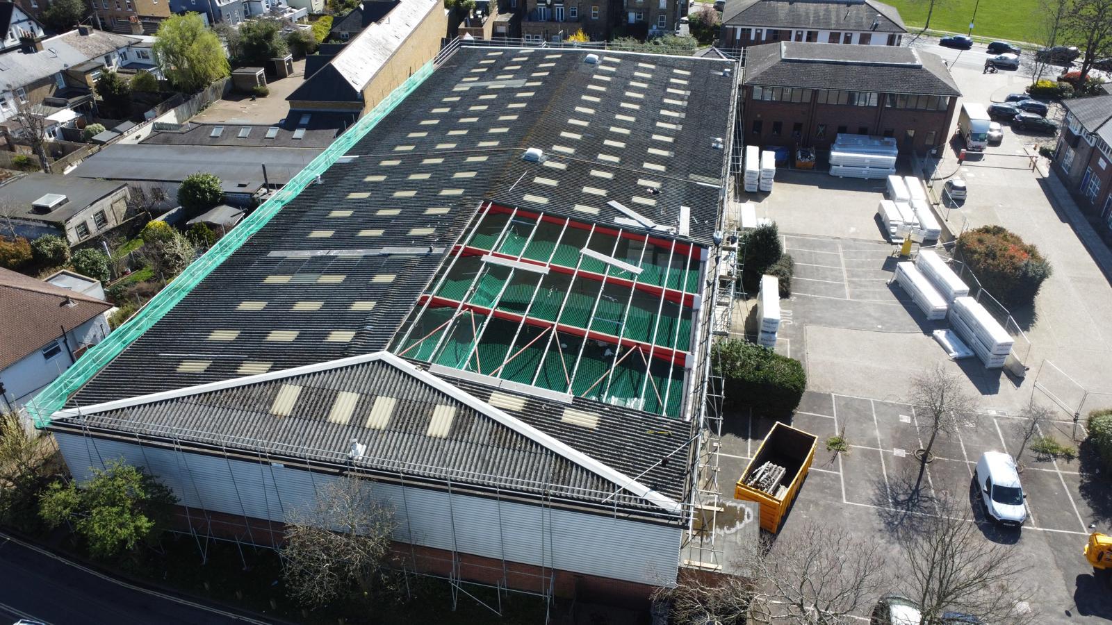 Aerial view of a commercial asbestos cement roof refurbishment with scaffolding, edge protection and waste skip on site