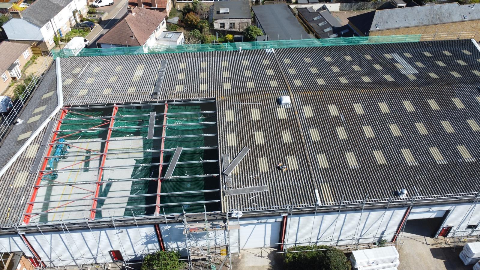 Aerial view of an industrial asbestos cement roof during replacement with scaffolding and crash-deck netting